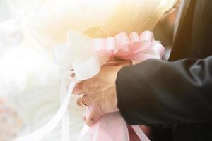 brudgum innehav reste sig blommor bukett med solljus i äktenskap. valentine dag för kärlek och firande begrepp. foto