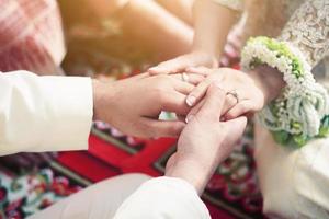 brudgum händer innehav brud händer med bröllop ringa i thai bröllop ceremoni traditionell. foto