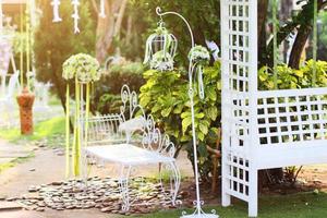vit fågelbur, stol dekoration med ro och vit blommor hängande dekoration i trädgård för bröllop ceremoni foto