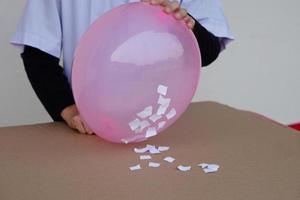 närbild studerande do vetenskap experimentera handla om statisk el från rosa ballong och bitar av papper. begrepp, vetenskap projekt arbete aktivitet. inlärning förbi håller på med. utbildning. foto