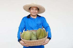 stilig asiatisk man jordbrukare bär hatt, blå skjorta, innehar korg av Durian frukter. begrepp, lantbruk ockupation. thai jordbrukare växa Durian frukt som ekonomisk och exportera frukt produktion foto