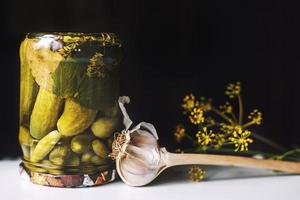 inlagd gurkor i en glas burk med vitlök och dill på en mörk bakgrund. omvänd burk med gurkor stänga foto