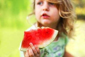 söt liten flicka innehav en bit av vattenmelon stänga i de trädgård i sommartid foto