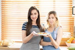 två caucasian kvinnor matlagning pizza tillsammans i de kök. de begrepp av Hem kokta mat och HBTQ relationer. familj och mångfald begrepp. HBTQ kärlek. foto