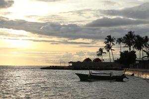 silhuett av en fiskares båt och en kokos träd på de strand med en solnedgång bakgrund foto
