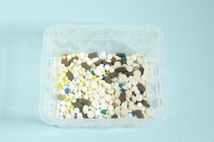 behållare med piller. flerfärgad och vit piller i en transparent låda. piller på en blå bakgrund. foto
