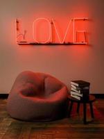 litet läshörn med en puff och ett litet bord som är upplyst med ett neonskylt med ordet kärlek, 3d framför foto