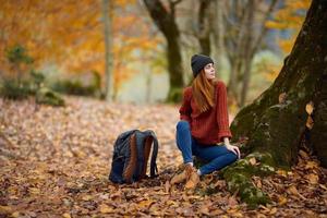 en kvinna i värma kläder i de falla sitter nära en träd i de skog foto