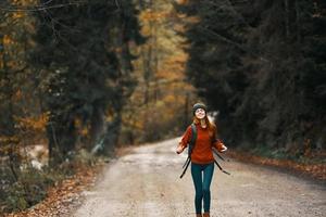 kvinna med ryggsäck på de väg i de skog i höst landskap lång träd modell foto