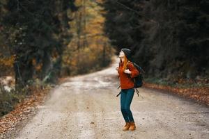 Lycklig kvinna vandrare med ryggsäck promenader på de väg i höst skog foto