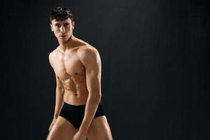 attraktiv atletisk man i svart shorts mörk bakgrund foto