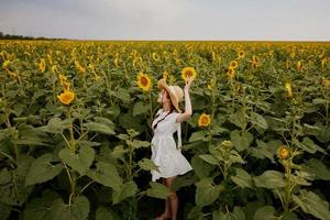 kvinna porträtt i en sugrör hatt i en vit klänning en fält av solrosor lantbruk sommar tid foto