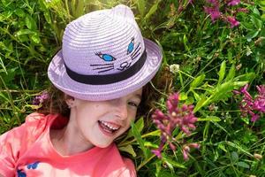 porträtt av en barn i en hatt med hans ansikte täckt i sommar liggande i de gräs och vilda blommor. hatt med ögon och öron tycka om en katt, sommar tid, frihet foto