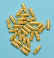 transparent medicinsk kapslar med gul granulat inuti på en blå bakgrund, tabletter för behandling, vitaminer foto