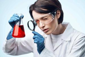 kvinna laboratorium assistent ser genom en förstorande glas på en kemisk lösning analys diagnostik foto