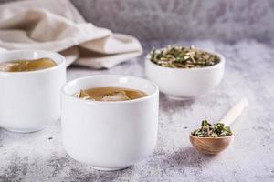 kall grön japansk hojicha te med is i koppar och torr te i en skål på de tabell foto