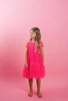 caucasian flicka av sju år gammal i en ljus rosa barbicore stil klänning på en rosa bakgrund foto