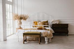 interiör av en modern vit sovrum, en dubbel- säng med kuddar och höst dekor, torkades blommor i en vas foto