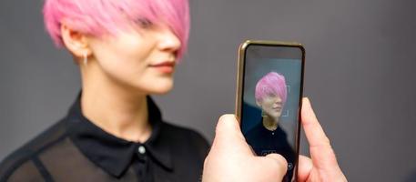 man frisersalong händer tar bild på smartphone av henne klient kort rosa frisyr. foto