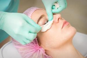 ung kvinna tar emot ögonhår avlägsnande procedur och tar bort mascara med en bomull svabb och pinne i en skönhet salong. foto