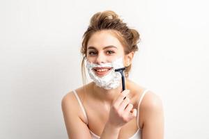 porträtt av skön ung leende caucasian kvinna rakar ansikte med rakapparat på vit bakgrund. foto
