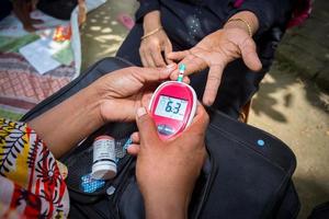 kvinna kontroll socker nivå med glukometer använder sig av en blod prov på narsingdi, bangladesh. lära sig till använda sig av en glukometer. begrepp av diabetes behandling. foto