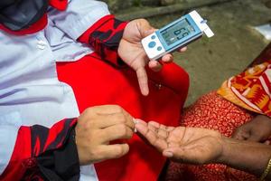 kvinna kontroll socker nivå med glukometer använder sig av en blod prov på narsingdi, bangladesh. lära sig till använda sig av en glukometer. begrepp av diabetes behandling. foto
