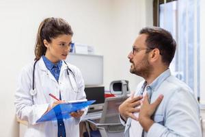 erfaren läkare diskuterar med patient hans privat medicinsk fil. ung man kontroll upp med hans md, och hört handla om de sätt av hans hälsa behandling och hälsa försäkring. foto