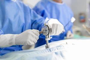 kirurger händer stänga upp utför kirurgi. kirurg använder sig av borra maskin under procedur. doktorer är bär skyddande arbetskläder i rörelse rum. foto
