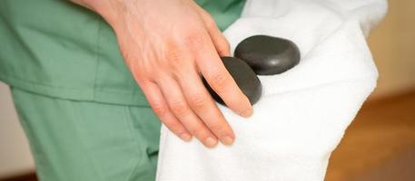 stänga upp av massörens hand våtservetter svart massage stenar med en vit handduk. foto