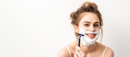 porträtt av skön ung leende caucasian kvinna rakar ansikte med rakapparat på vit bakgrund. foto