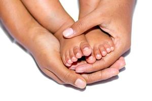 de mjuk ben av en bebis placerad på de handflatan av de mors två händer på en vit bakgrund. foto