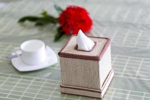 rå fiber Färg handgjort servett låda på de dining tabell med en röd blomma och en vit tekopp. vävnad papper låda på restaurang. foto