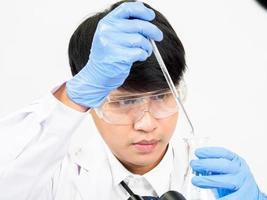 asiatisk man studerande forskare eller läkare se hand innehav i reagens blandning laboratorium i en vetenskap forskning laboratorium med testa rör av olika storlekar i laboratorium kemi labb vit bakgrund. foto