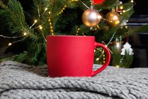 tom röd råna med jul träd på bakgrund, matta te eller kaffe kopp med jul och ny år dekoration, vertikal falsk upp med keramisk råna för varm drycker, tom gåva skriva ut mall. foto