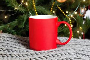 tom röd råna med jul träd på bakgrund, matta te eller kaffe kopp med jul och ny år dekoration, vertikal falsk upp med keramisk råna för varm drycker, tom gåva skriva ut mall. foto