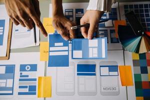 stänga upp ux utvecklare och ui designer brainstorming handla om mobil app gränssnitt trådmodell design på tabell med kund kortfattat och Färg koda på modern office.creative digital utveckling byrå foto
