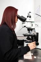 ung kvinna forskare analyserar en patient prov under en fluorescens mikroskop i en genetik laboratorium foto