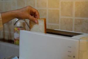 de hushållerska sätter bröd in i de brödrost till förbereda frukost för alla i de hus. mjuk och selektiv fokus. foto