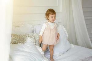 söt liten flicka Hoppar på vit säng foto