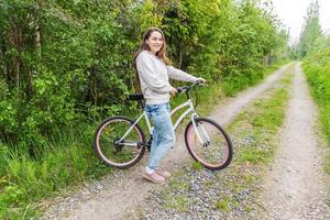 ung kvinna ridning cykel i sommar stad parkera utomhus. aktiva människor. hipster flicka koppla av och ryttare cykel foto