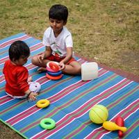 två Lycklig Pojkar i samhälle parkera, Lycklig asiatisk bröder vem är leende lyckligt tillsammans. bröder spela utomhus i sommar, bäst vänner. litet barn bebis pojke spelar med hans Lycklig bror i de trädgård foto