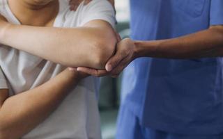 läkare eller fysioterapeut arbetssätt granskning behandla skadade ärm av idrottare manlig patient, stretching och träning, håller på med de rehabilitering terapi smärta i klinik. foto