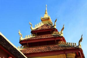 gyllene naga på konst tak av buddist tempel med blå himmel i wat pha den där luang tempel vientiane provins, laos foto