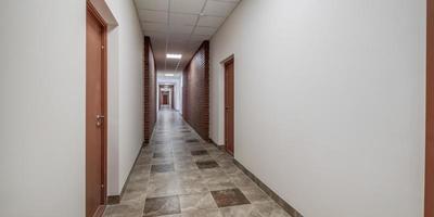 panorama i tömma lång korridor med röd tegel väggar och dörrar i interiör av modern kontor foto