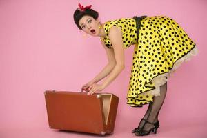 skön utvikningsbrud flicka öppnas en retro resväska. retro kvinna i gul polka punkt klänning. de känsla av överraskning. foto