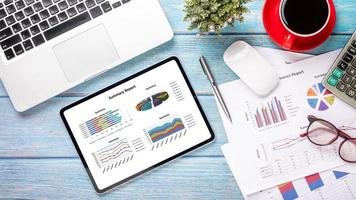 läsplatta med diagram och rapporter, kalkylator, penna, anteckningsbok och kaffe på kontor skrivbord arbetsplats. topp se platt lägga med kopia Plats. foto