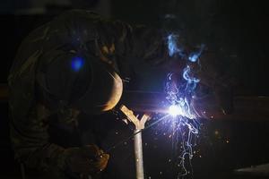 svetsare på arbete. man i en skyddande mask. de svetsare gör sömmar på de metall. gnistor och rök när svetsning. foto