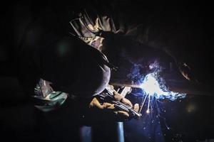 svetsare på arbete. man i en skyddande mask. de svetsare gör sömmar på de metall. gnistor och rök när svetsning. foto