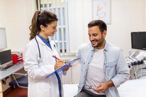 erfaren läkare diskuterar med patient hans privat medicinsk fil. ung man kontroll upp med hans md, och hört handla om de sätt av hans hälsa behandling och hälsa försäkring. foto